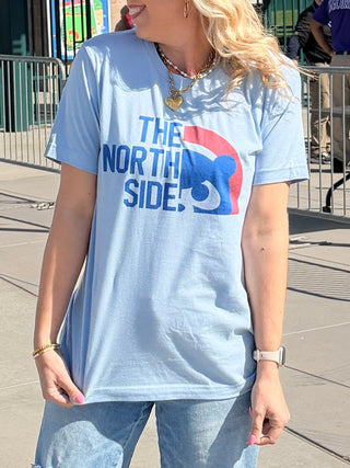 Person wearing a blue t-shirt and jeans standing on a sidewalk with a stadium in the background
