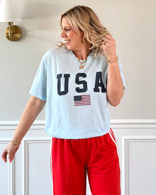 Woman wearing a light blue 'USA' t-shirt with an American flag graphic and red pants.