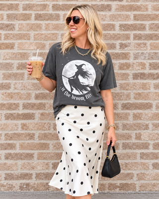 girl wearing if the broom fits with flying witch graphic tee with white and black polka dot skirt holding an ice coffee and a black purse