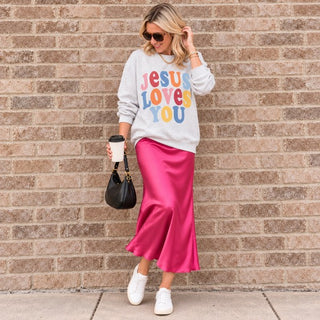 Woman wearing the Jesus Loves You Christian sweatshirt in Ash gray with a pink satin midi skirt
